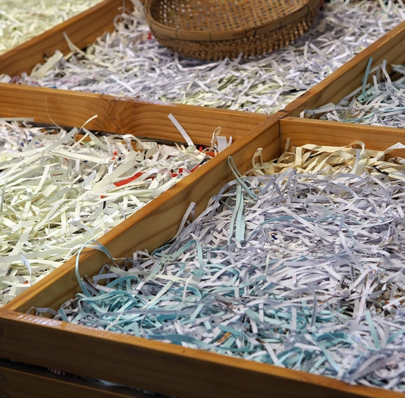 A wooden display case features various sections filled with colorful shredded paper, showcasing the attention to detail synonymous with Confidential Paper Shredding Services, while a small wicker basket perches neatly on top.